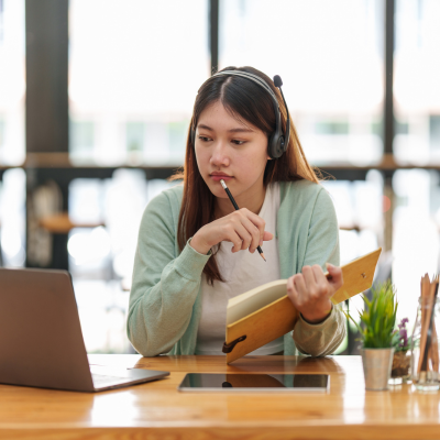 woman studying at a laptop with a book in her hand